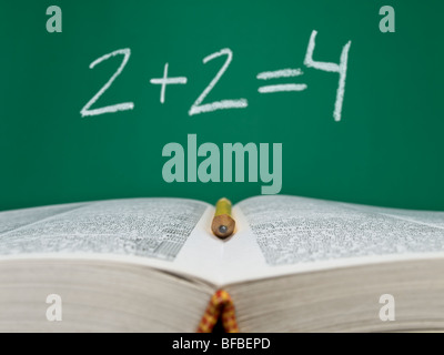 2  + 2  = 4 écrit sur une ardoise avec un livre ouvert et un crayon sur le premier plan. Banque D'Images