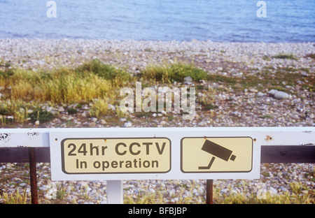 Plage de galets rugueux avec les mauvaises herbes et au-delà la mer avec grille rouillée et image emblématique de huis clos et d'avertissement à l'opération de vidéosurveillance 24h/24 Banque D'Images