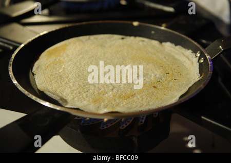 Une poêle sur une plaque de cuisson à gaz avec une crêpe à la cuisson. Banque D'Images