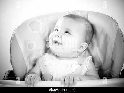 Petite Fille en rose haut allaitement et être nourris en bleu et jaune chaise haute Banque D'Images