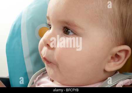 Petite Fille en rose haut allaitement et être nourris en bleu et jaune chaise haute Banque D'Images