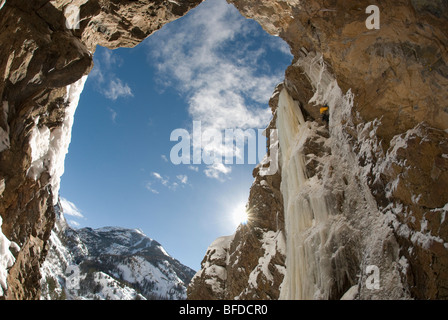 Vue de dessous comme un grimpeur sur glace monte une cascade gelée sur un pur rock face. Banque D'Images