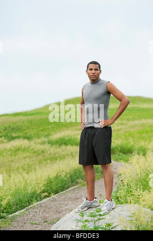 Jeune homme debout sur la roche suite à l'utilisation sur piste de gravier à travers un champ vert vif à l'esprit, le Dakota du Sud. Banque D'Images