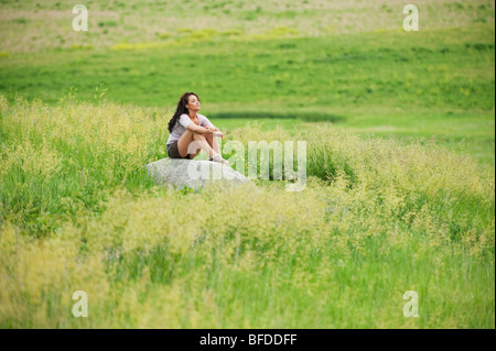 Jeune femme de l'emplacement sur la roche dans un champ vert vif à l'esprit, le Dakota du Sud.