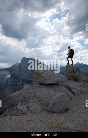 Une femelle randonneur sur les rochers de granit sur la North Dome au Yosemite National Park, avec demi-dôme en arrière-plan. Banque D'Images