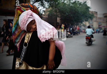 Une jeune fille ouïghoure dormir sur le bras de sa mère dans une rue de Kashgar, Xinjiang, Chine. Banque D'Images