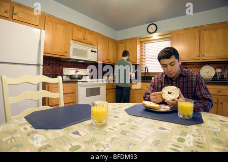 Deux jeunes hommes assis à une table de cuisine et prêt à manger le petit déjeuner. Banque D'Images