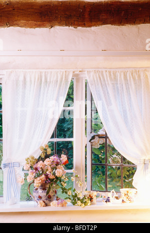 Voile blanc les rideaux à la fenêtre de la chambre chalet avec vase de roses on windowsill Banque D'Images