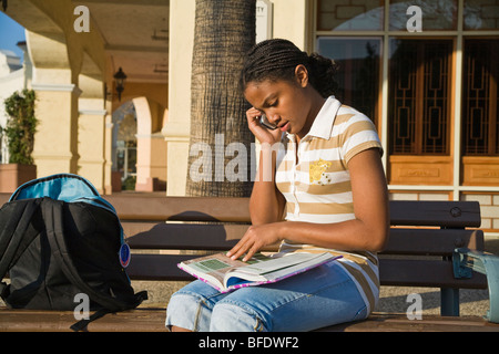 African American girl 13-15 ans talking on mobile phone alors que faire ses devoirs. California United States MR Banque D'Images