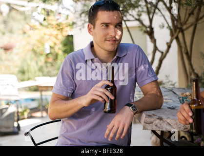 Jeune homme ayant la bière sur le bar, piscine dans l'arrière-plan. Banque D'Images