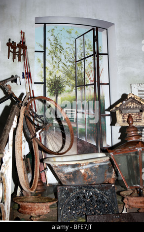 Tableau des éléments en vente dans un marché d'antiquités d'intérieur en face d'une peinture murale dynamique de portes-fenêtres s'ouvrant sur patio et jardins Banque D'Images