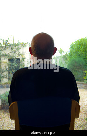 Un homme assis dans son jardin d'affichage grâce à une grande fenêtre Banque D'Images