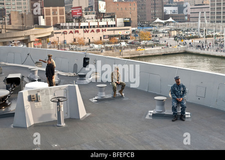 2 jeunes hommes prennent une pause sur le gaillard d'immaculée de l'USS New York tandis qu'un agent donne un tour à un visiteur Banque D'Images