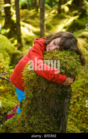 Girl hugging moss couverts stump, Parc Provincial Naikoon, Queen Charlotte Islands, British Columbia, Canada Banque D'Images