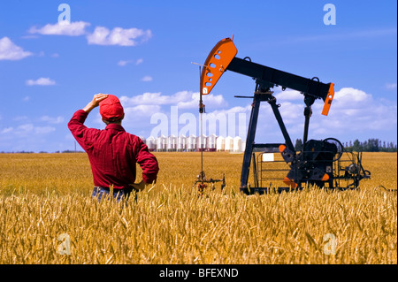 L'homme donne sur un champ de blé prêt de la récolte avec une pompe à huile et jack en arrière-plan des cellules à grains près de Sinclair Manitoba Canada Banque D'Images