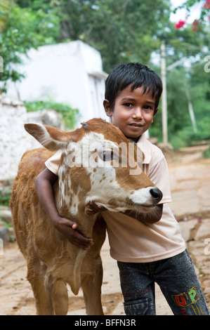 Jeune Indien boy hugging un veau dans un village de l'Inde rurale. L'Andhra Pradesh, Inde Banque D'Images