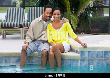 Une happy African American man and woman couple dans la trentaine assis avec les pieds dans une piscine. Banque D'Images