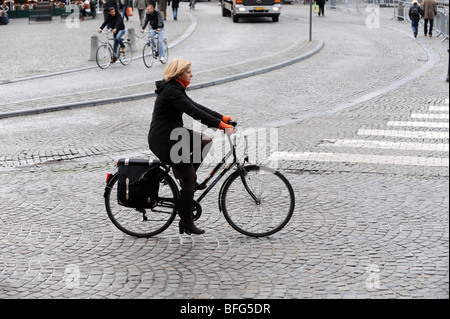 Une jeune femme à vélo sur les rues pavées de Bruges en Belgique Europe Banque D'Images