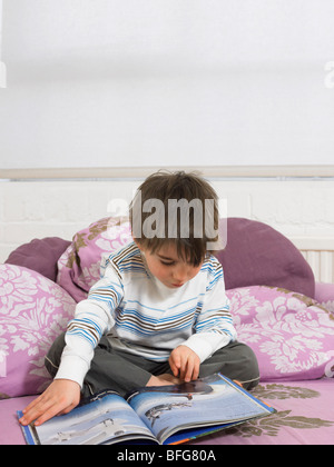 Boy (5-6) reading book on couch in living room Banque D'Images