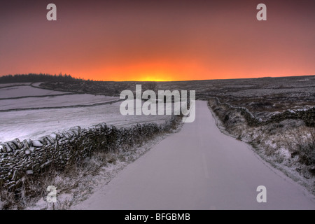 Une route couverte de neige mène à un lever de soleil sur le bord de la Pennines, UK. Banque D'Images