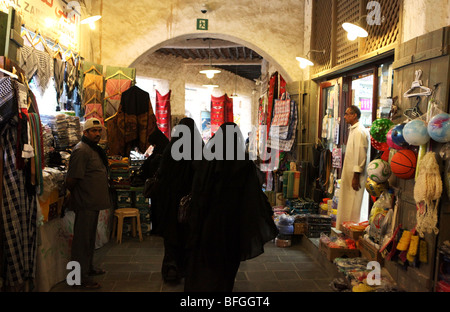 Trois femmes arabes Qatari couverts shopping dans la zone couverte de Souq Waqif, Doha, Qatar, tandis que les commerçants attendre par leurs étals. Banque D'Images