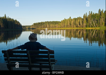 Man relaxing on park bench avec une vue sur le lac. Deux Mile Lake, Parc provincial Duck Mountain, Manitoba, Canada Banque D'Images