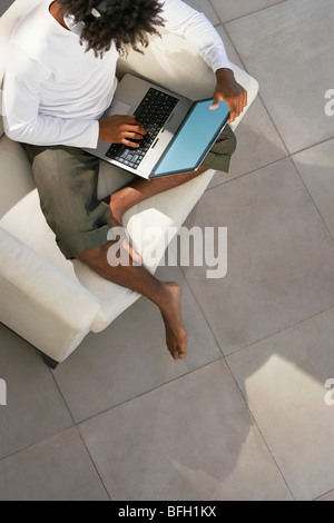 Jeune homme assis sur le canapé à l'extérieur à l'aide d'ordinateur portable et l'écoute de la musique via des écouteurs, overhead view Banque D'Images