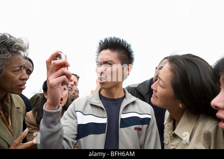 Angry Young Man holding mobile phone in crowd Banque D'Images