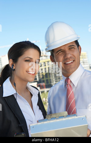 Businessman in hardhat montrant de l'écouteur avec presse-papiers Banque D'Images