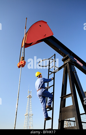 Worker climbing pump jack avec de l'huile de forage en arrière-plan à découvrir du pétrole canadien Museum de Devon, en Alberta, Canada. Banque D'Images