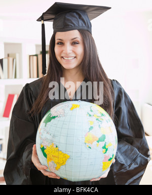 Mixed Race graduate in cap and gown holding globe Banque D'Images