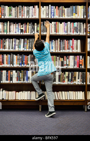 Boy Reaching for livre sur l'étagère de bibliothèque Banque D'Images