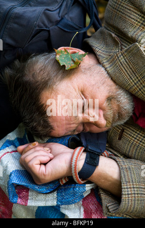 Un homme sans abri / un sommeil agitée endormi sur un banc. Une feuille tombant a atterri sur son oreille. Banque D'Images