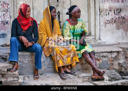 La Tanzanie, Zanzibar, Stone Town. Trois jeunes femmes se détendre sur une pierre pas dans Stone Town. Banque D'Images