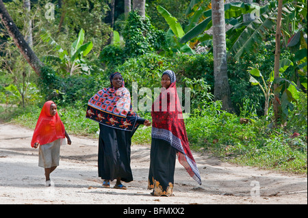 La Tanzanie, Zanzibar. Deux femmes pause pour chat sur la route près de Mangapwani comme une jeune fille passe. Banque D'Images