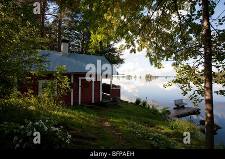 Extérieur d'une petite cabine de sauna en bois rouge près d'un lac calme à plat en été, Finlande Banque D'Images