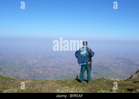 Un guide local avec un fusil sur son épaule à la recherche sur les collines et vallées ci-dessous dans le montagnes du Simien Banque D'Images