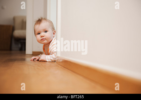 Bébé couché sur le plancher d'oeil autour d'un coin Banque D'Images