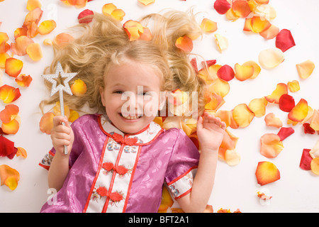 Petite fille avec Magic Wand se prélassant parmi les pétales de fleurs Banque D'Images