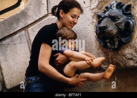 Bébé de 16 mois avec sa maman jolie Faustine pied dans une fontaine Banque D'Images