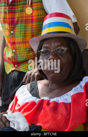 Femme vêtue de noir Couleurs célébrant la Journée nationale de l'indépendance à St Johns, Antigua avec son mari debout derrière Banque D'Images