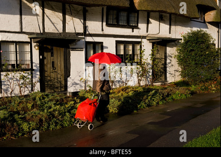 Une femme avec un parapluie rouge et panier balade par temps humide en face de Tudor cadre en bois Chalets, Wendover, au Royaume-Uni. Banque D'Images