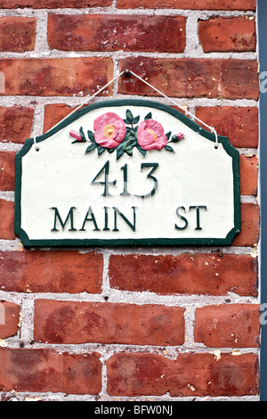 La pendaison de charme green & white metal house number sign with pink roses sauvages sur un vieux mur de brique dans le nord de New York Rosendale Banque D'Images