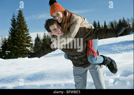 Young woman riding piggyback sur jeune homme de scène d'hiver Banque D'Images