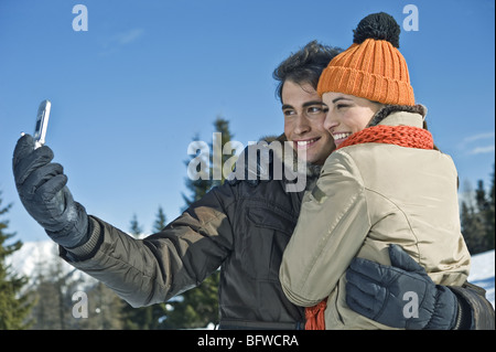 Couple photographing themselves with mobile phone appareil photo en scène d'hiver Banque D'Images