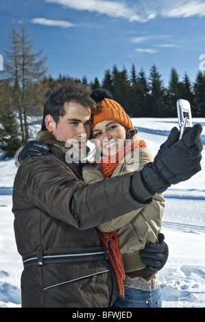 Couple photographing themselves with mobile phone appareil photo en scène d'hiver Banque D'Images