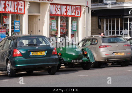 Trois voitures en stationnement sur une rue en face de magasins. Deux voitures modernes un sandwich classic vintage Bentley. Banque D'Images