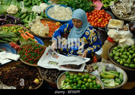 Le malais de Malaisie ou femme lisant un journal quotidien sur l'étal de légumes du marché, Marché Central, Kota Bahru, Malaisie Banque D'Images