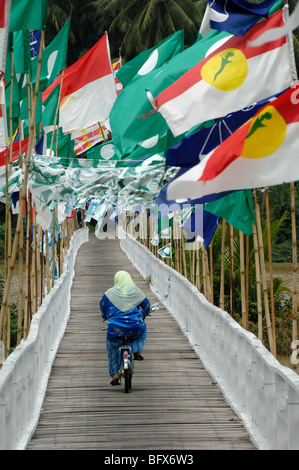 Femme musulmane de Malaisie malaisien ou du vélo à travers le pont de pied en bois couvert de drapeaux de l'élection, Kuala Terengganu, Malaisie Banque D'Images