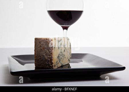 Coin de Stilton sur une plaque noire accompagnée d'un verre de vin rouge. Banque D'Images